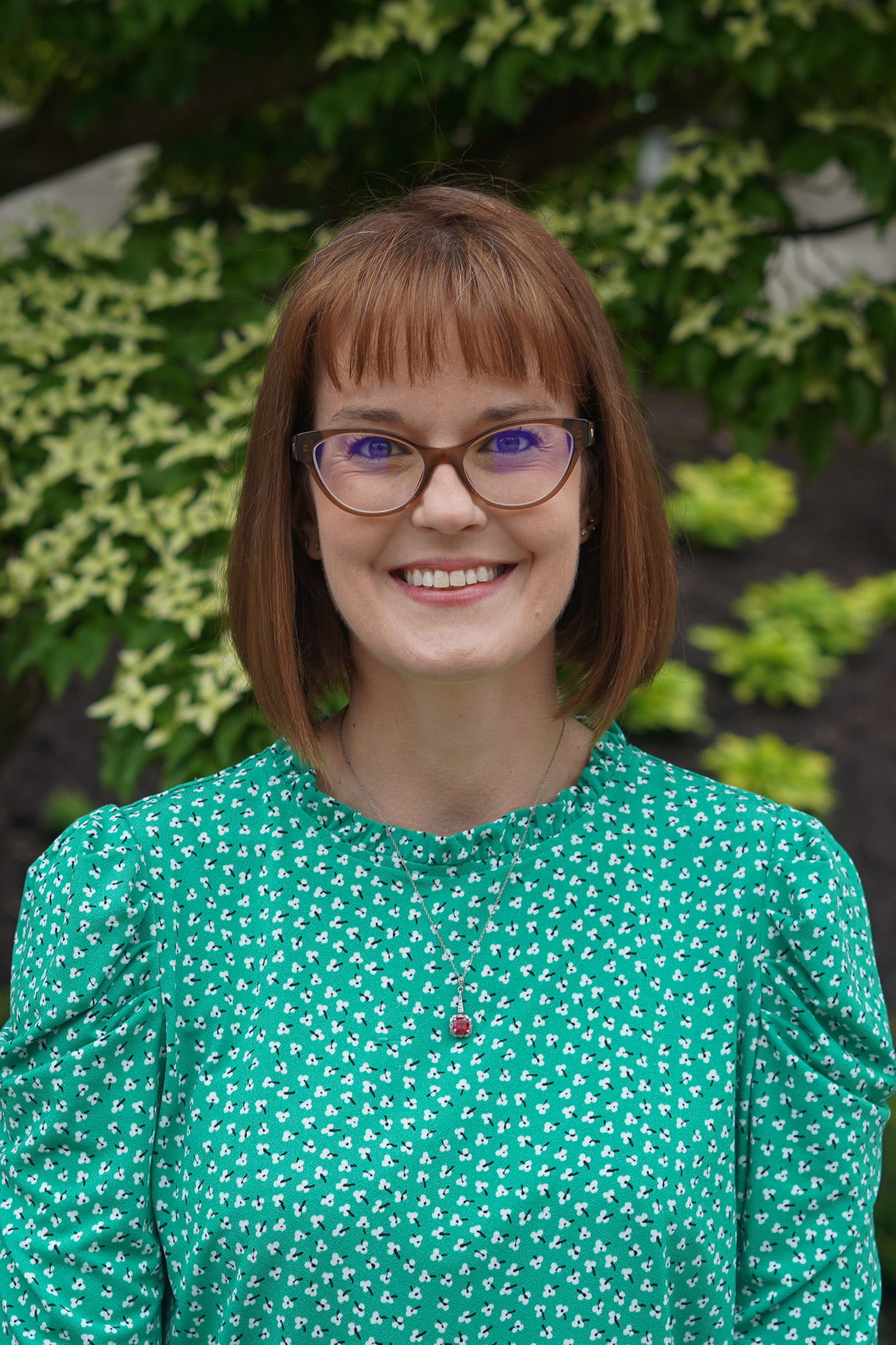 Woman in a green shirt standing in front of shrubbery