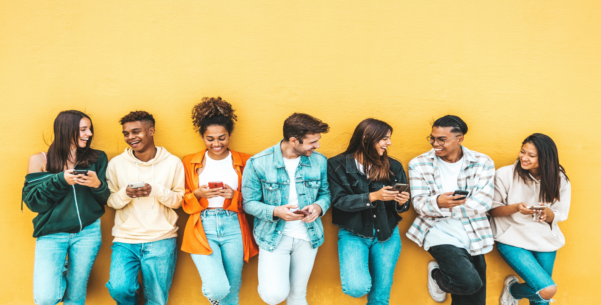 Group of students with cell phones standing near wall